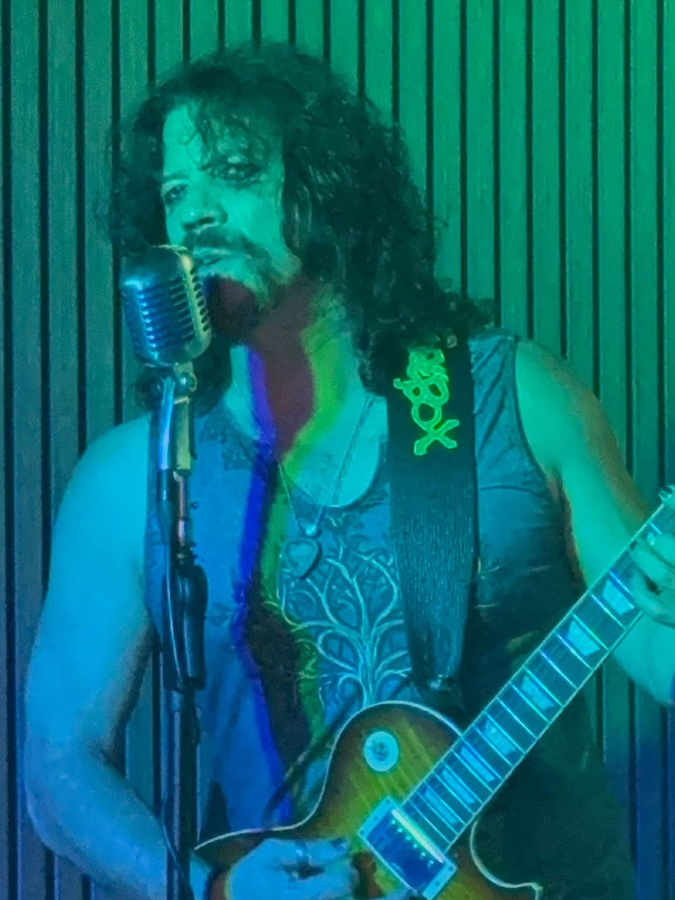 Mike Ruggirello plays guitar and sings in blue and green light